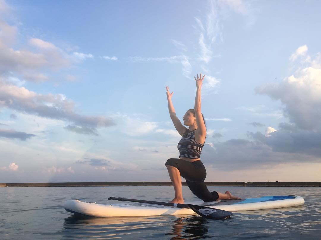 Woman in yoga gear doing a yoga pose on a surfboard in the water.