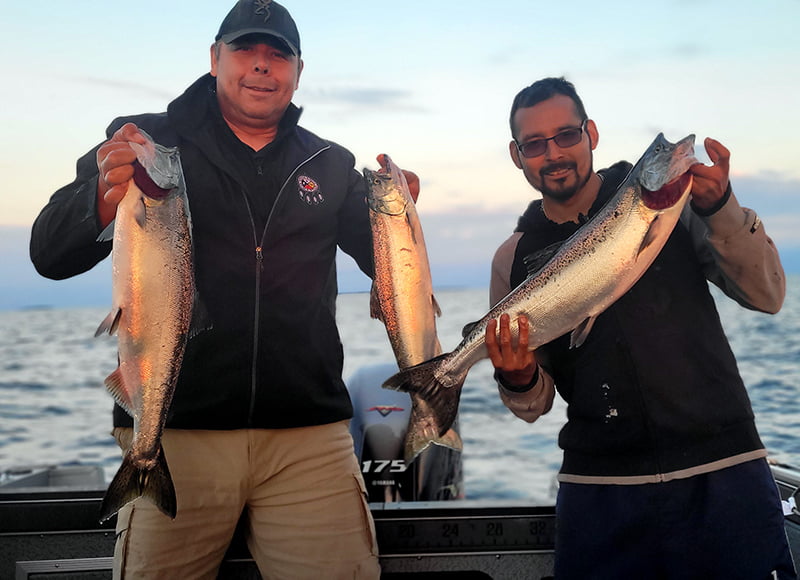 Two men on a boat holding up fish they have caught.