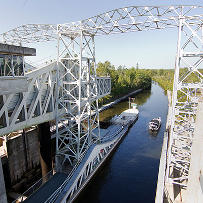 The Kirkfield Lock; a towering white metal lattice hydraulic lift over a glassy waterway with a boat in it on a summer day.
