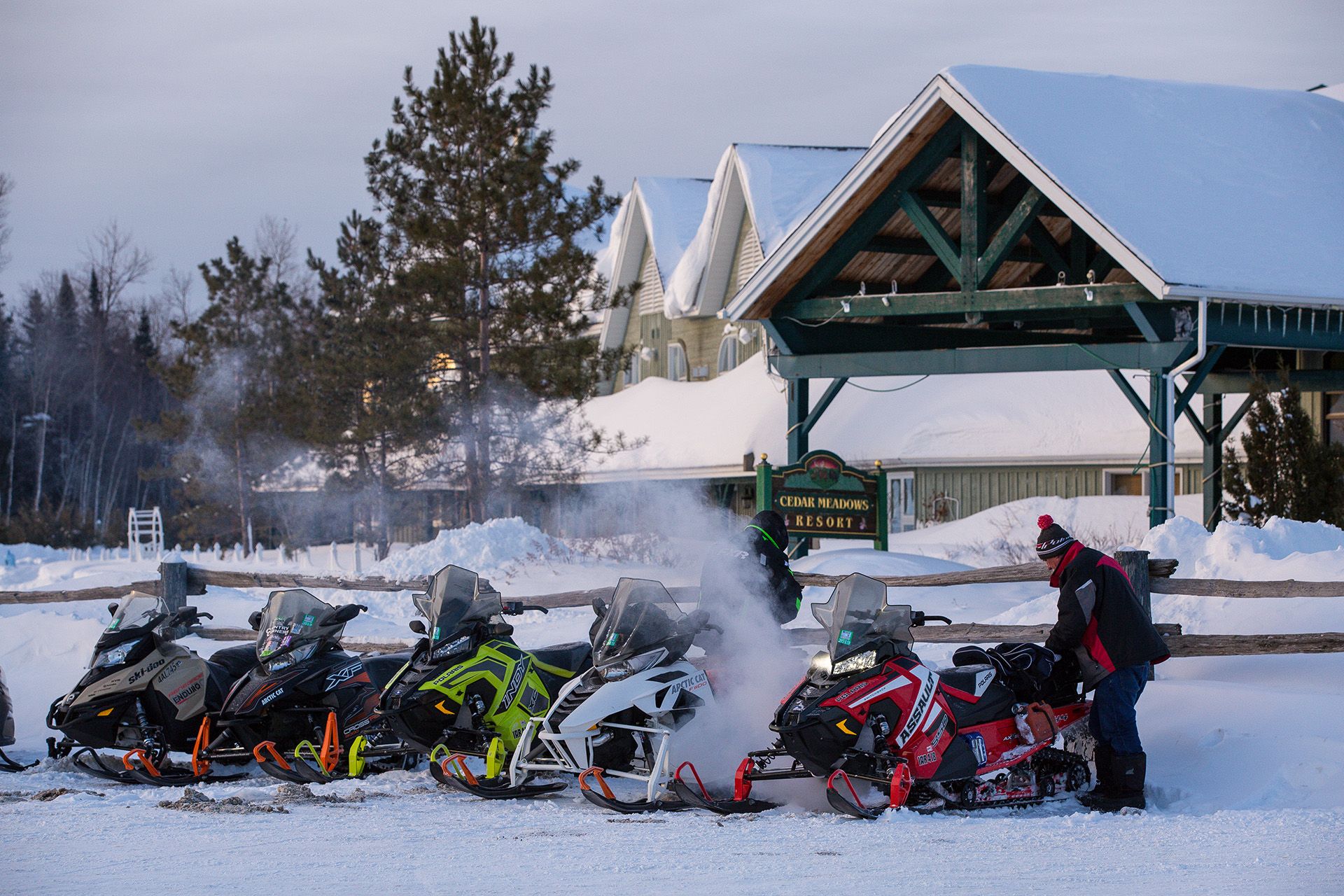 A rider checks a line of snowmobiles parked outside the Cedar Meadows Resort on a snowy morning.